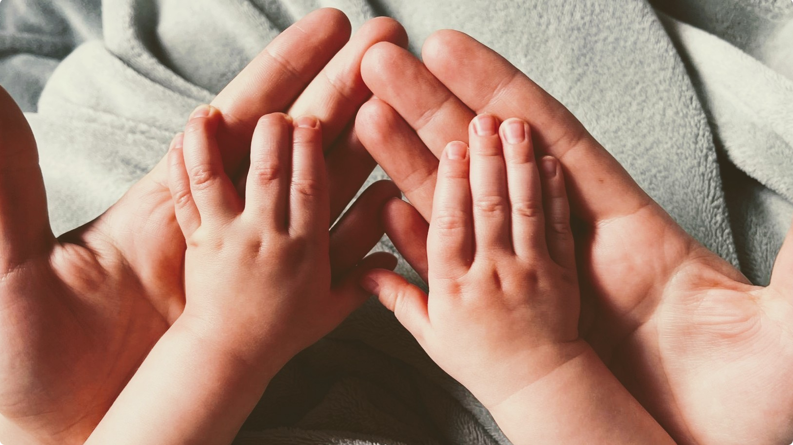 Babyhände liegen in den Händen von einem Erwachsenen